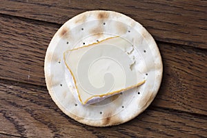 One water biscuit with cheese, on wood from above.