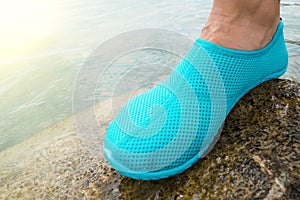 One Water shoe / blue swimming shoe on rocks in water on beach. Closeup detail of the feet of a woman wearing water shoes standing