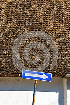 One way street european traffic sign with white arrow on blue surface with vintage roof tile pattern in background