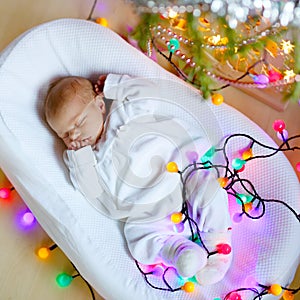 One week old newborn baby girl sleeping near Christmas tree