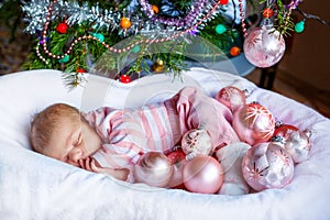 One week old newborn baby girl with pink balls near Christmas tree