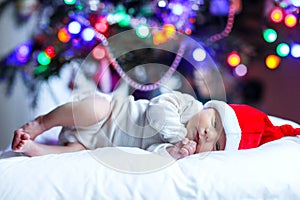 One week old newborn baby in Santa hat near Christmas tree