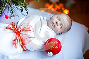 One week old newborn baby wrapped in blanket near Christmas tree