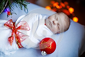 One week old newborn baby wrapped in blanket near Christmas tree