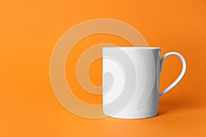 One white ceramic mug on orange background. Space for text