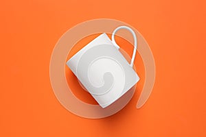 One white ceramic mug on orange background, top view