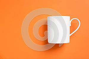 One white ceramic mug on orange background, top view. Space for text