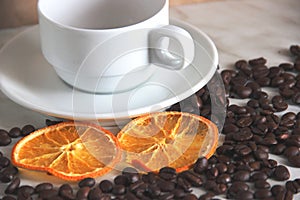 One white classic Cup with saucer on the table, roasted coffee beans and dried orange slices