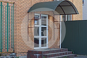 One white closed door with glass on a bricks brown wall with steps threshold