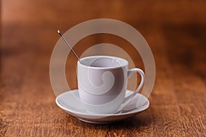 One white coffe Cup with spoon on white saucer on dark brown wooden background