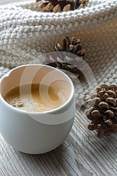 One white cup of coffee is standing on the wooden table. Black coffee on the wood with several cones