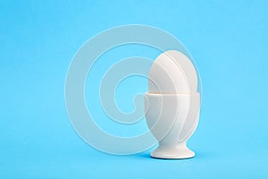 One white egg in an egg cup on blue background