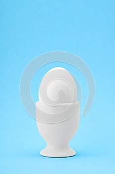 One white egg in an egg cup on blue background