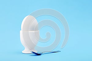 One white egg in an egg cup on blue background
