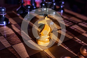 One white knight staying against full set of black chess pieces. Closeup of chessboard with wooden pieces on table in sunlight,