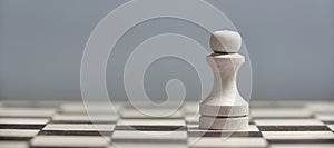 One white pawn close-up on a chessboard on a gray background. Background in blur