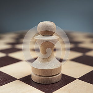 One white pawn close-up on a chessboard on a gray background. Background in blur