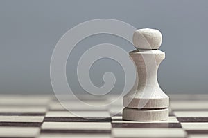 One white pawn close-up on a chessboard on a gray background. Photo with copy space.