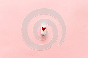 One white pills on pink background with red heart shape, cardiac medications or femine cure