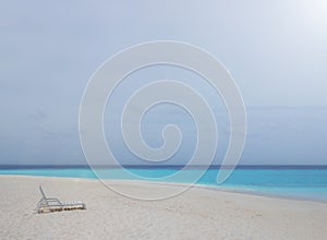 One white plastic beach chair on white sand beach with bright clear blue sky and colorful sea water.