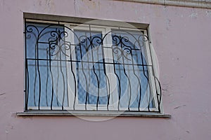 One white window with black iron bars on a pink wall with cracks