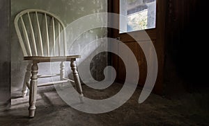 One white wooden vintage chair standing in an empty room under the light from the door