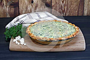 One whole spinach and feta cheese quiche on a cutting board.