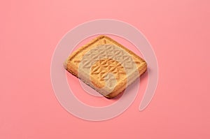 One whole square cookie lies on pink desk on kitchen