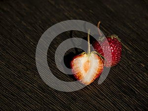 One whole strawberry and one half strawberry on a dark wooden surface