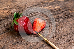 One whole strawberry and one half strawberry with paint brush on a dark wooden surface with space to write on the right