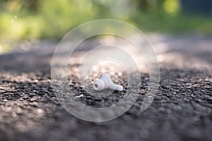 One wireless headphones is lost and lies on the asphalt sidewalk, outdoors.