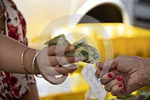 One woman hands another woman a twenty dollar bill against a blurred background