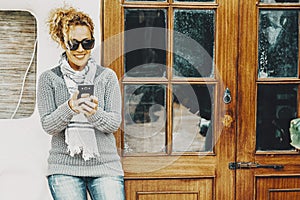 One woman outside door home using mobile phone wifi connection writing with a smile. Modern female people use cellular outdoor in