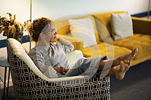 One woman sitting on the chair at home with legs up and barefoot comfort. Female people at home in linving room relax and enjoy photo