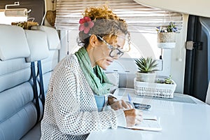 One woman sitting inside modern motorhome alternative tiny house and write travel notes on the table. People living vanlife on the