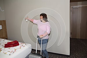 One woman with a suitcase is standing in a hotel room near the bed with keys in her hand, concept of vacation, business trip