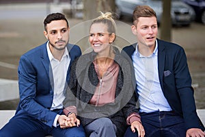 One woman and two men sitting on bench togehter