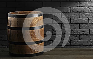 One wooden barrel on table near brick wall.