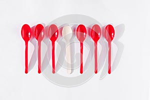 One wooden and five red plastic spoons on white background flat lay. Zero waste ecological concept, health planet.