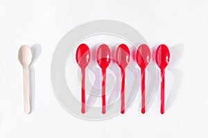 One wooden and five red plastic spoons on white background flat lay. Zero waste ecological concept, health planet.