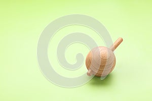 One wooden spinning top on light green background, space for text. Toy whirligig