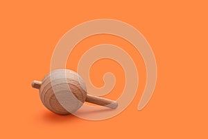 One wooden spinning top on orange background, space for text. Toy whirligig