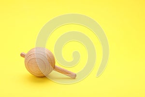 One wooden spinning top on yellow background, space for text. Toy whirligig