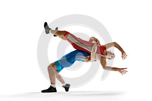 One wrestler in red uniform thrown by opponent in blue, both captured mid-fall in motion against white studio background