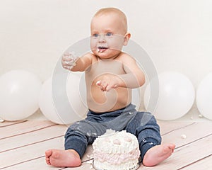 One year baby birthday party. Baby eating birthday cake. The boy on a light background with ballons celebrates and smash the cake