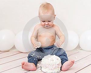 One year baby birthday party. Baby eating birthday cake. The boy on a light background celebrates and smash the cream cake