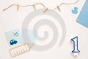 One year baby concept. A blue candle in the shape of one lies on a white background with children`s accessories. Boy birthday