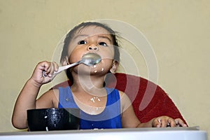 One 1 year old Asian baby boy learning to eat by himself by spoon, messy on baby dining chair at home