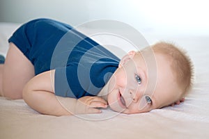 One year old baby boy in blue t-shirt lying in the bed on white bed sheet.