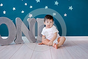 One year old baby boy celebrates birthday near silver letters ONE on blue background with stars